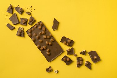 A chocolate bar with scattered pieces on a yellow background