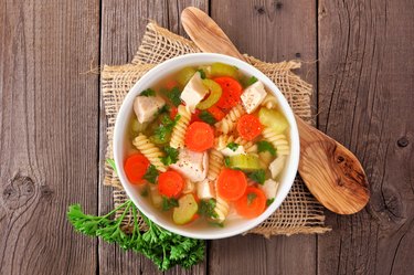 Homemade chicken noodle soup with vegetables, top view on a wood background