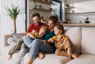 parents and two children sitting on a sofa at home looking at a tablet to view their at-home DNA test kit results