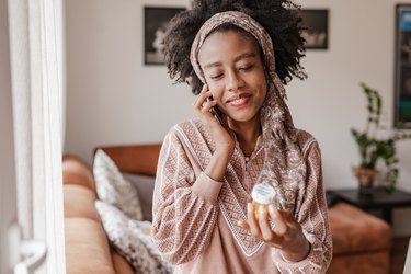 a person with a black afro wearing a light brown sweater and headband and holding a bottle of prescription pills because they're taking spironolactone for acne
