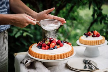 Woman preparing fresh fruits and berries cake with gluten-free sugar