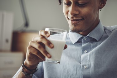 Young adult wearing a blue button-down shirt at home holding a glass of milk to neutralize spicy food in the stomach
