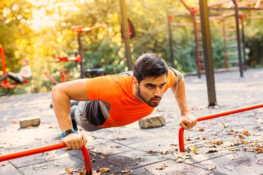 Person doing push-ups in a park outside using push-up bars.