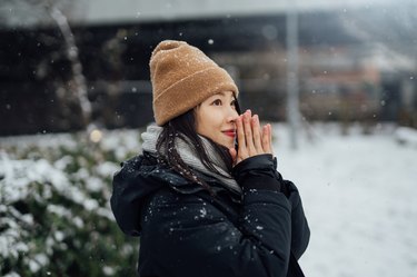 Close up of person in the snow wearing a heavy black coat and tan beanie, with wet hair in the cold