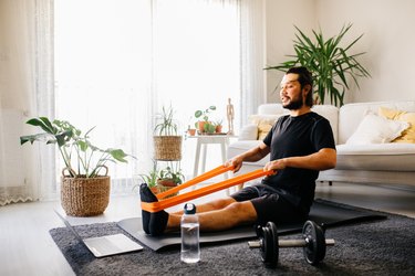 man doing seated resistance band exercises on the floor of his living room, watching a computer