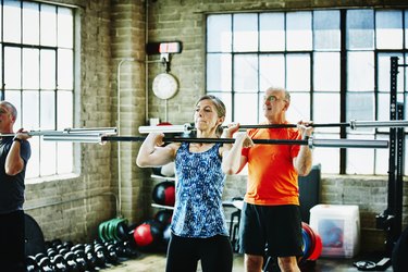 Mature athletes doing a barbell warm-up before they begin lifting weights.