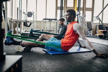Two young adults stretching and strengthening their ankles with resistance bands in the gym.