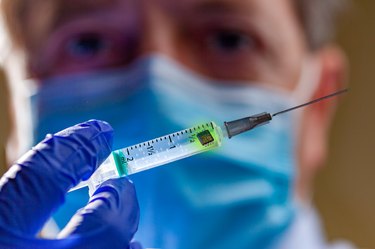 A vaccine syringe held in front of health care worker's masked face to show COVID vaccine conspiracy theory concept