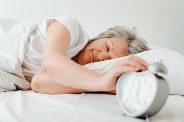 Older adult sleeping on their side, holding an alarm clock