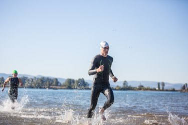 Triathletes wearing triathlon suits running out of the water during a race.