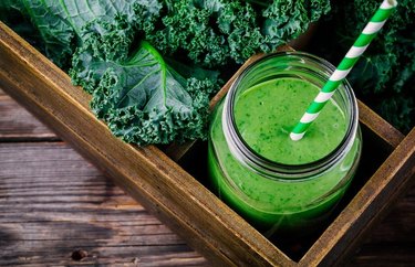 peaches and greens smoothie in a mason jar with a green and white striped straw